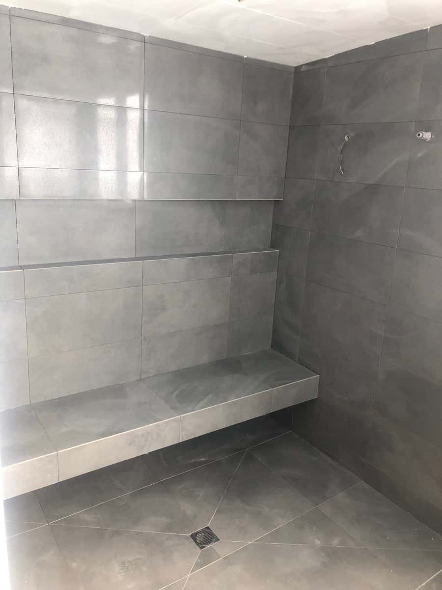 Dark grey large-format tiled shower area with a built-in bench seat and floor falls to the drain.