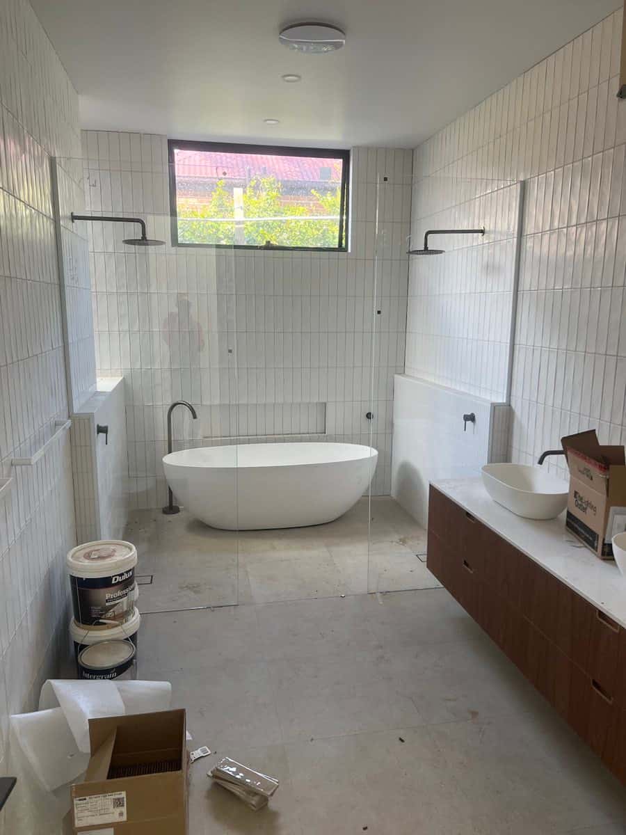 Bathroom with a freestanding bath, twin shower layout, and vertically stacked wall tiles.