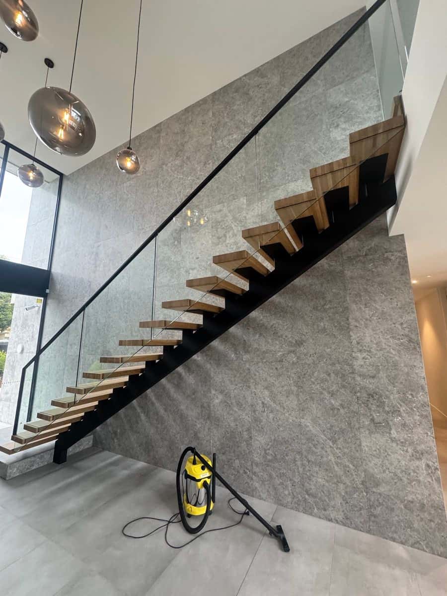 Floating timber staircase set against a full-height grey stone-look tiled feature wall.