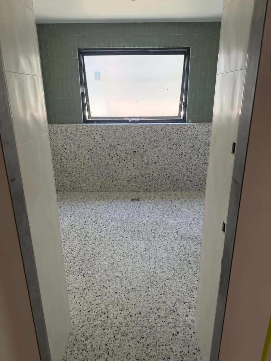 Bathroom with terrazzo floor and wall finishes framed by green tiles around a window.